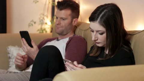 Couple sitting on couch on their cell phones ignoring, unhappy relationship. 4K Stock Footage 155470358
