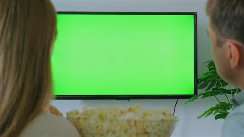 Couple sitting on couch watching TV with green screen, enjoying Video stock 284123778