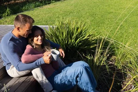 Couple sitting on deck steps in yard, woman holding white mug, man wrapping arm, Stock Photos