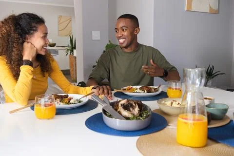 Couple sitting at dining table man in olive-tee woman in yellow-top holding Stock Photos