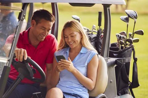 Couple Sitting In Golf Buggy On Course With Woman Using Mobile Phone Fotos Stock