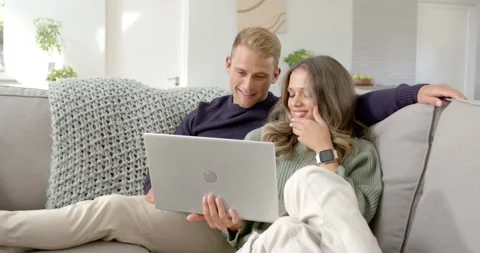 Couple sitting on grey sofa, man with silver laptop explaining screen content Video stock 344536922