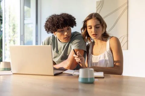 Couple sitting at home dining table, leaning over laptop and notebook near Fotos Stock