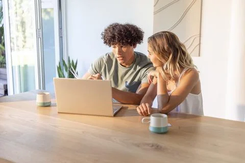 Couple sitting at home dining table, wearing T-shirt and tank top, working on Stock Photos