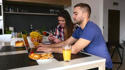Couple sitting in the kitchen. Man is using laptop. Girl is using smartphone. Stock Footage 61858015
