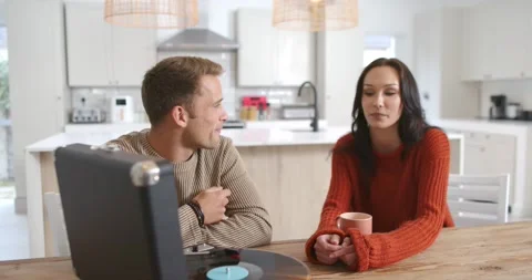 Couple sitting at kitchen table, man leaning in making point toward turntable, Stock-Footage 344405505