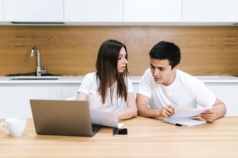 Couple is sitting at kitchen table, use laptop and taking care of utility bil Stock Photos
