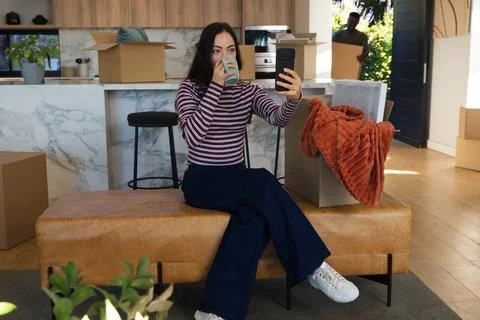Couple sitting on leather bench in kitchen, woman taking phone selfie sipping Stock Photos