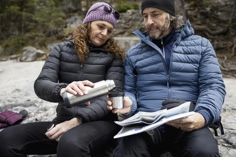 Couple sitting looking at map and having drink on rock Fotos Stock