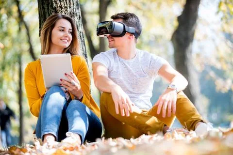 Couple sitting outside using various tech gadgets Stock Photos