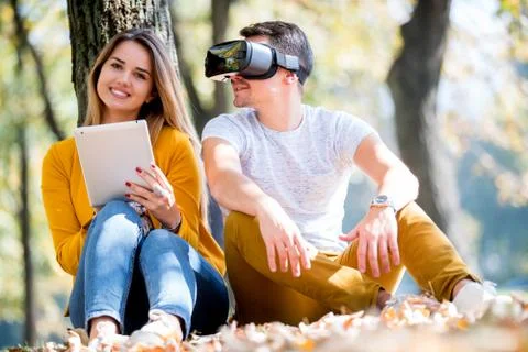 Couple sitting outside using various tech gadgets Stock Photos
