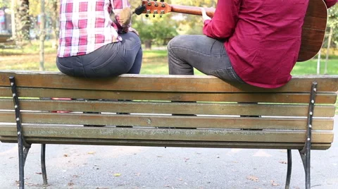 Couple sitting on park bench, man playing guitar while woman singing Stock Footage 59556948