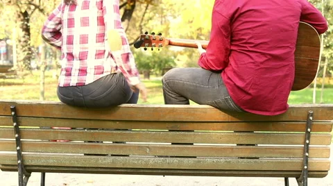 Couple sitting on park bench, man playing guitar while woman singing Stock Footage 59556965