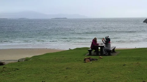 Couple sitting at picnic table on ocean beach and having a fun conversation Stock Footage 101542646