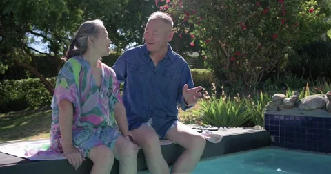 Couple sitting poolside on towel, man speaking, leaning, wrapping arm comforting Stock Footage 339559150
