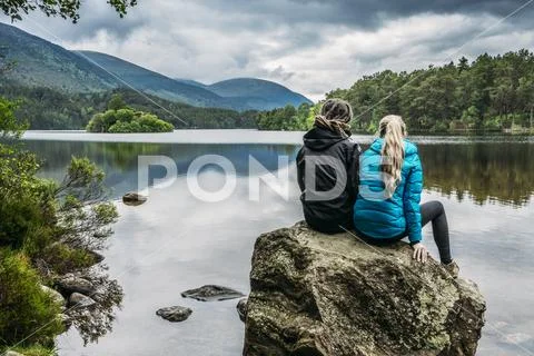 Couple sitting on rock looking at tranquil lake, Loch an Eilein, Scotland Stock Photos