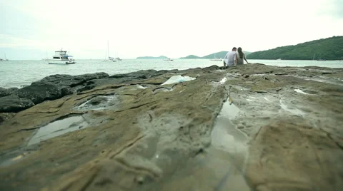 Couple sitting on the rocks at a beach Stock Footage 64254344