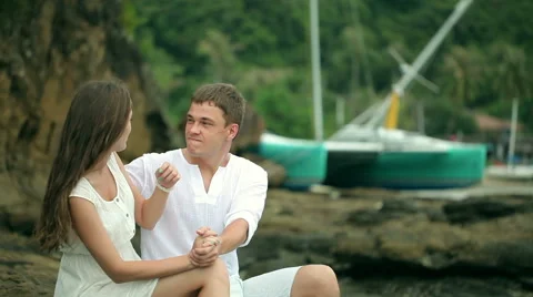 Couple sitting on the rocks at a beach Stock Footage 64254395