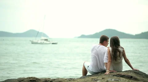 Couple sitting on the rocks at a beach Stock Footage 64254431