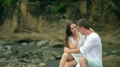 Couple sitting on the rocks at a beach Stock Footage 64254449