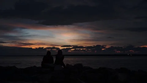 A couple sitting on rocks beach side together enjoy sunset view Stock Footage 101062705