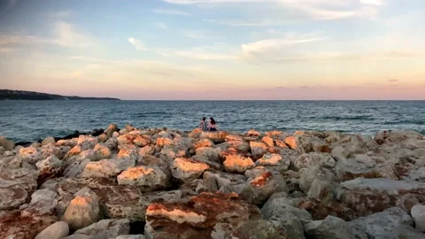 Couple Sitting On Rocks On The Beach At Sunset. A  Beautiful Sunset. Stock Footage 150403591