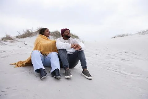 Couple sitting on sand dune wrapped in mustard-yellow shawl, man wearing Stock Photos