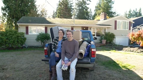 Couple sitting side by side at back of van by house, looking at camera and 動画素材 88162428