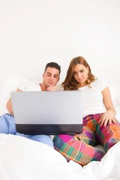 Couple sitting side by side in bed relaxing with computer Stock Photos