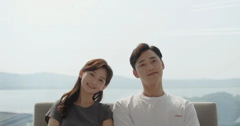 Couple is sitting side by side on the couch and looking at the camera Stock Footage 100941988