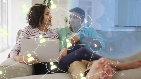 Couple sitting on sofa browsing laptop, single tech icon appearing over man, Stock Footage 333301319