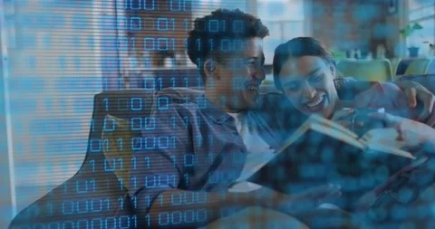 Couple sitting on sofa reading book sharing laugh, binary code overlay fading Stock Footage 318688340