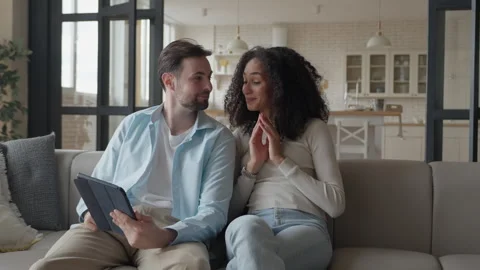 Couple Sitting On Sofa Using Tablet Together, Woman Pointing At Screen, Smiling Stock Footage 306699269