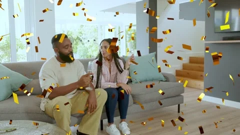 Couple sitting on sofa when raising flutes, gold confetti falling around, Stock Footage 333448943
