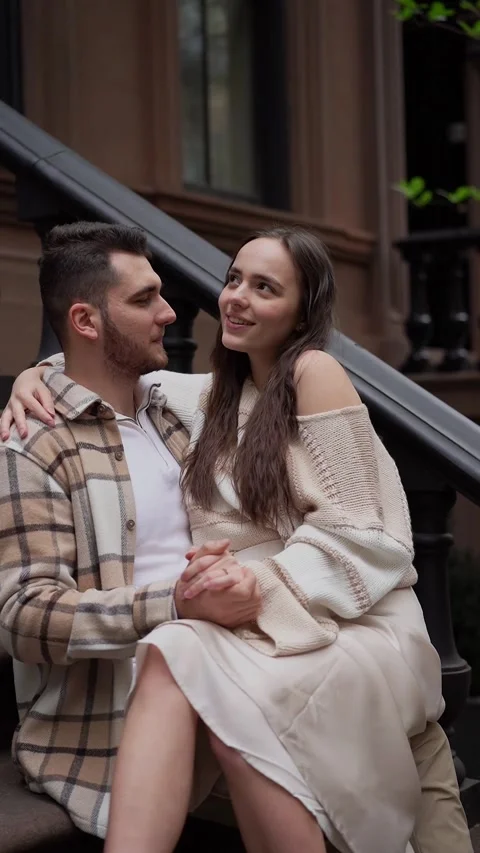 Couple sitting on steps of brownstone building, enjoying each others company 스톡 동영상 290842963