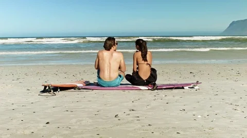 Couple sitting on surfboards on beach Stock Footage 76521647