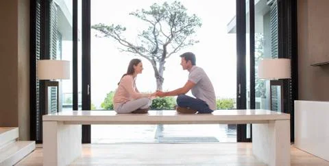 Couple sitting on table face to face and holding hands, tree seen through patio Stock Photos
