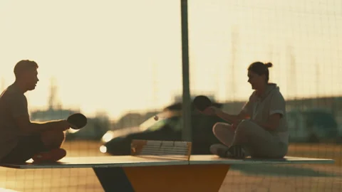 Couple sitting on a table playing ping pong at sunset Stock Footage 332506662
