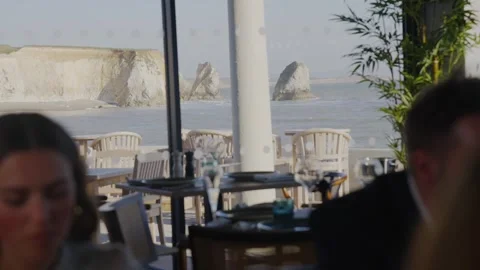 A couple is sitting at a table in a restaurant overlooking the ocean Stock Footage 306576338