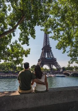 Couple sitting on wall looking at Eiffel Tower in distance in Paris. Stock Photos