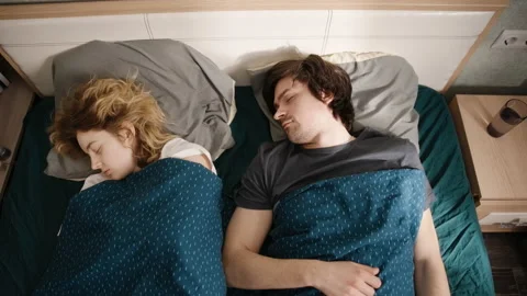 Couple sleeping in bed, young man wakes up, rubs face and looks at woman Vidéo 197488978