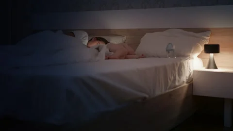 Couple sleeping peacefully in a dimly lit bedroom, cozy bedding and bedside lamp Stock Footage 341523369