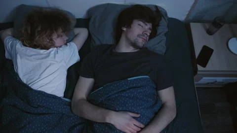 A couple sleeps in bed, the alarm clock rings on the phone, they wake up Vidéo 197367646