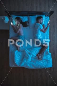 The couple with smartphone lay on the bed. night time view. from above Stock Photos