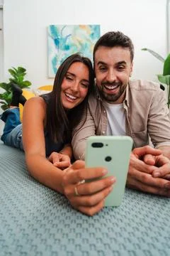 Couple smiles while taking a selfie with smartphone on bed during cozy home Stock Photos
