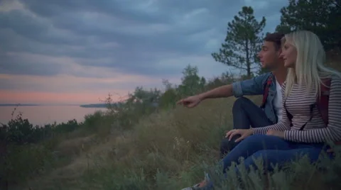 Couple smiling looking at landscape sitting on hill at sunrise Slow motion Stock Footage