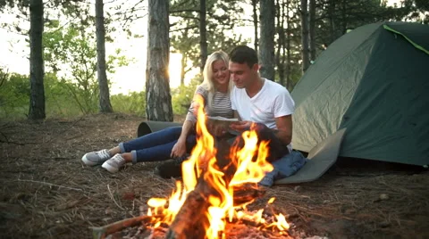 Couple smiling looking at map near bonfire in forest at sunset Slow motion Stock Footage 68115579