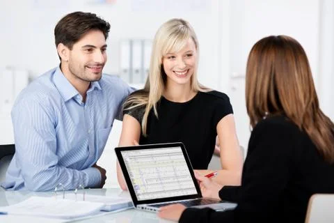 Couple smiling while looking at financial advisor at desk Stock Photos