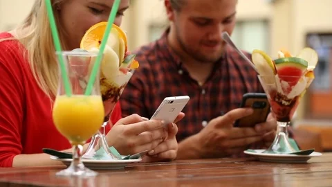 Couple smiling while texting on smartphones in the restaurant Stock Footage 77483892