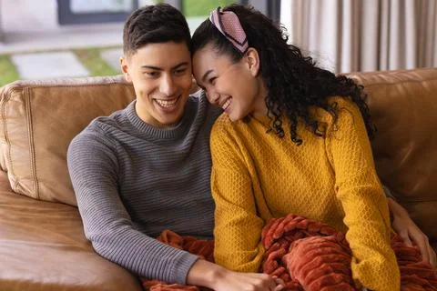 Couple snuggling under red throw blanket on brown leather couch in living room Stock Photos